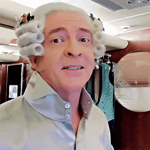 a man wearing a wig and buttons on his shirt looks at the camera