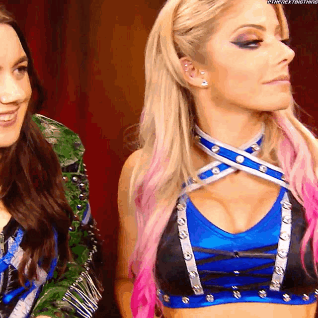 two women are standing next to each other with one wearing a blue top and the other wearing a green jacket