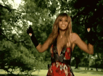 a woman wearing a red dress and black gloves is standing in a park .