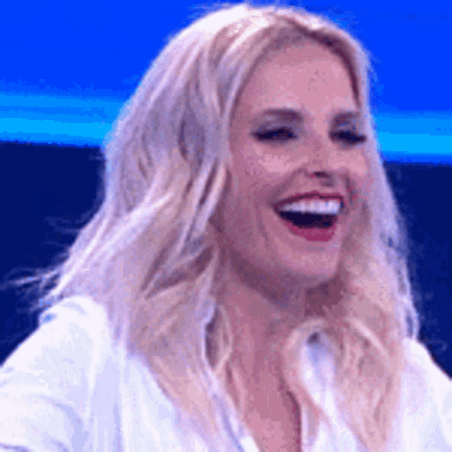 a woman with blonde hair and red lips is laughing with her mouth open .