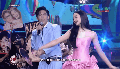 a man singing into a microphone while a woman in a pink dress stands next to him