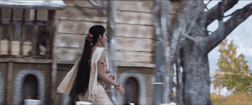 a woman in a white dress is walking in front of a wooden building
