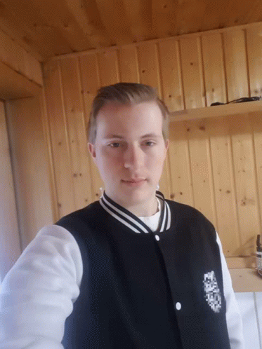 a young man wearing a black and white varsity jacket stands in front of a wood wall