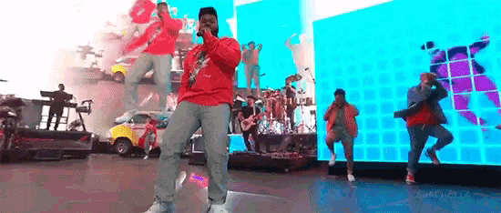 a man in a red shirt is singing into a microphone on a stage with a band behind him