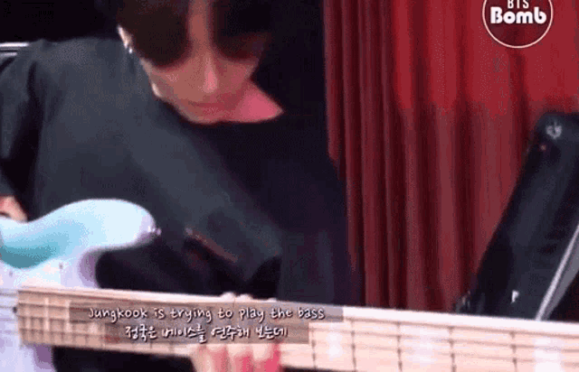 jungkook is trying to play the bass guitar in a video .
