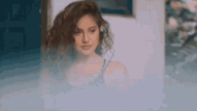 a woman with curly hair is standing in a room with a painting on the wall .
