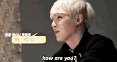 a young man with blonde hair is sitting at a table and talking to someone in a foreign language .