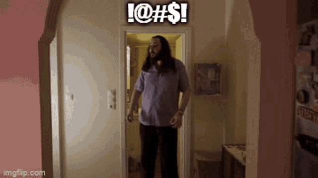 a man with long hair is standing in a hallway with a sign above him that says !@#$!