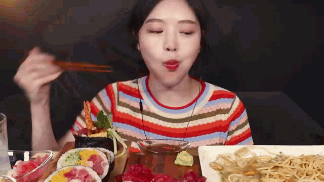 a woman in a striped shirt is eating sushi with chopsticks .