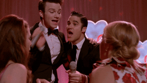 a man in a tuxedo is holding a microphone in front of a group of people