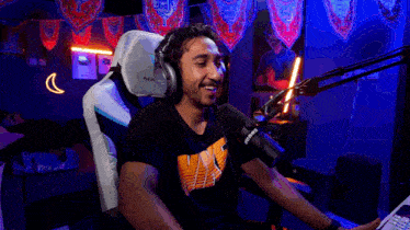a man wearing headphones and a nike shirt is sitting in front of a microphone and smiling .