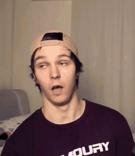 a young man wearing a baseball cap and a burgundy shirt that says moury makes a funny face