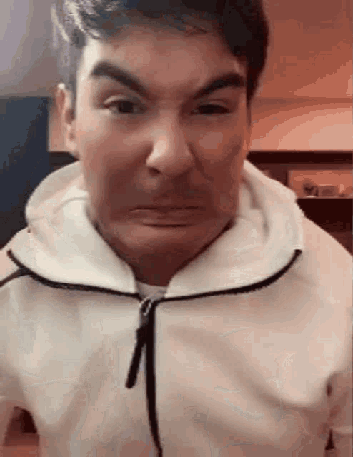 a man is making a funny face while wearing a white hoodie .