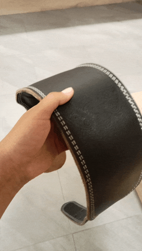 a person is holding a black leather belt with stitching