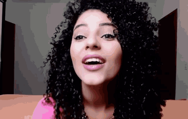 a woman with curly hair is wearing a pink shirt and necklace