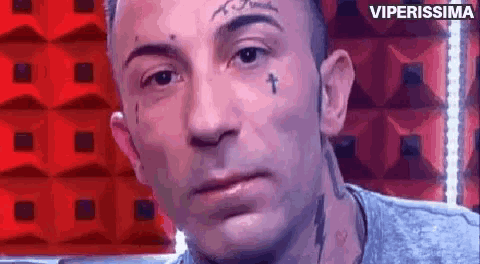 a man with a tattoo on his face and a cross on his forehead looks at the camera .
