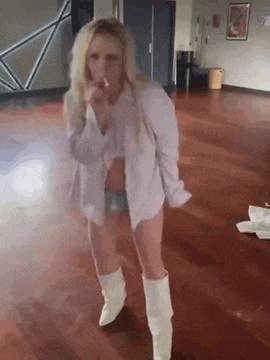 a woman in a white shirt and white boots is standing on a wooden floor in a room .