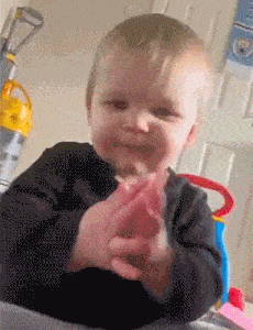 a baby is clapping his hands and smiling in front of a vacuum cleaner