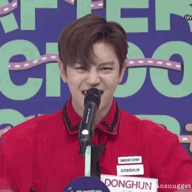 a young man in a red shirt is singing into a microphone with the name donghun on his name tag