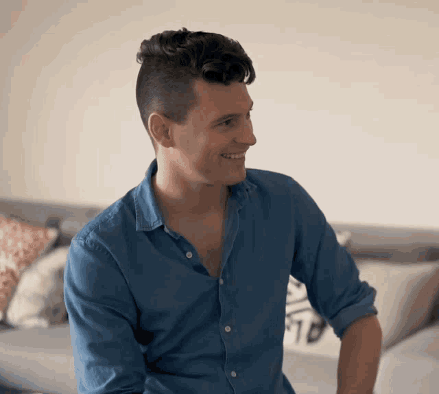 a man in a blue shirt is sitting on a couch and smiling