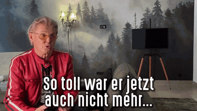 a man in a red jacket is sitting on a couch with the words so toll war er jetzt auch nicht mehr below him