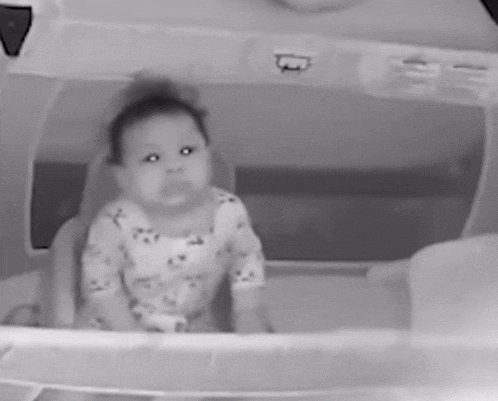 a black and white photo of a baby sitting in a crib