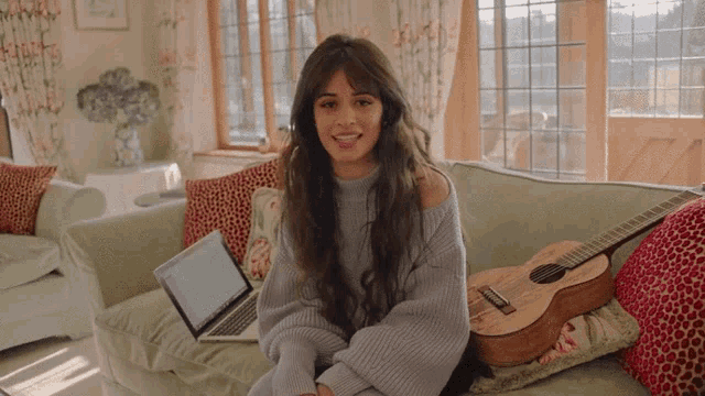 a woman is sitting on a couch with a guitar and a laptop