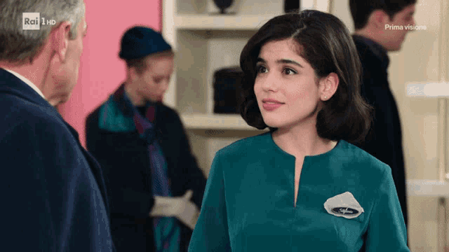 a woman in a green dress is talking to a man in a suit with rai hd in the corner