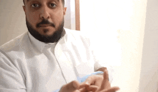 a man with a beard is wearing a white shirt and blue gloves and is holding something in his hands .