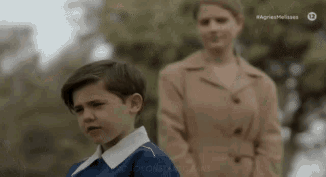 a young boy is standing next to a woman in a brown coat .