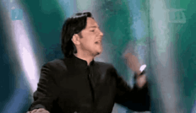 a man in a black suit is singing on a stage in front of a green wall .