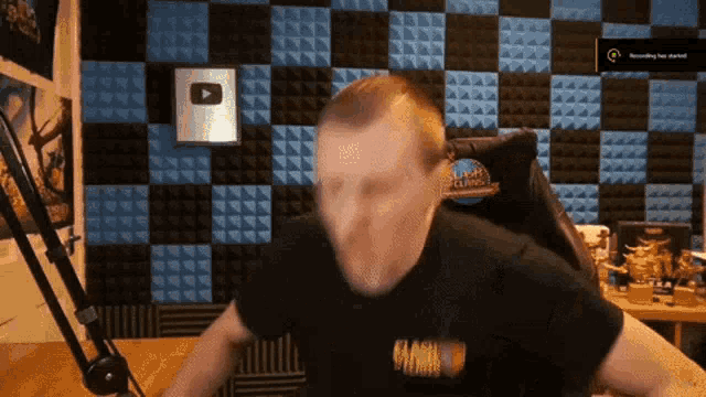 a man in a black shirt with the word gaming on it is standing in front of a checkered wall