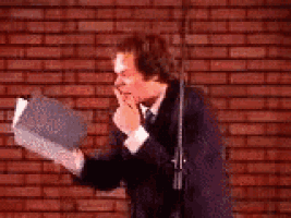 a man in a suit and tie is standing in front of a microphone holding a book .