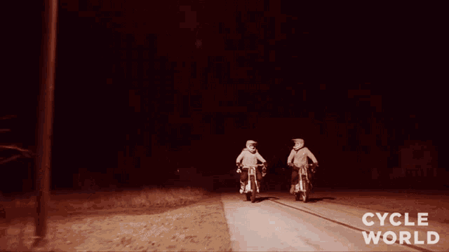 two people riding motorcycles in the dark with cycle world written on the bottom right