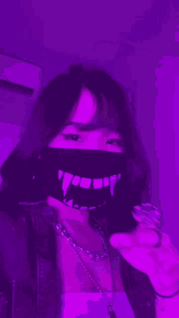 a girl wearing a mask with vampire teeth on it is standing in front of a purple background .