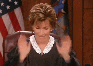 a woman in a judge 's robe is sitting in front of an american flag and clapping her hands .
