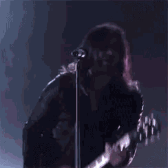 a person is singing into a microphone on a stage in front of a purple background .