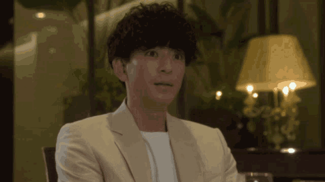 a man with curly hair is wearing a white jacket and white shirt