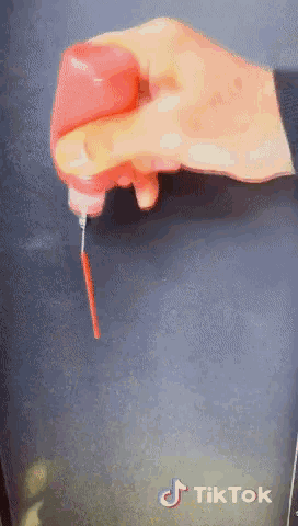 a hand is holding a red bottle with a screwdriver and a tiktok logo on the bottom