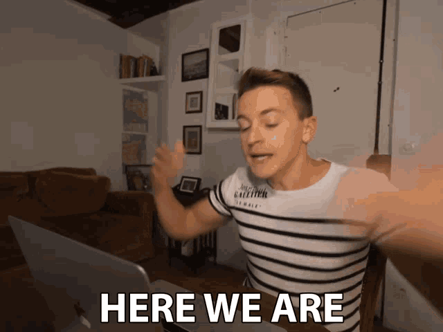 a man in a striped shirt says here we are in front of his laptop