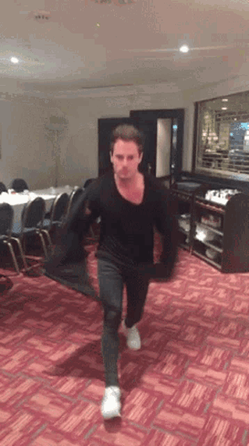 a man in a black shirt is running in a room with red carpet
