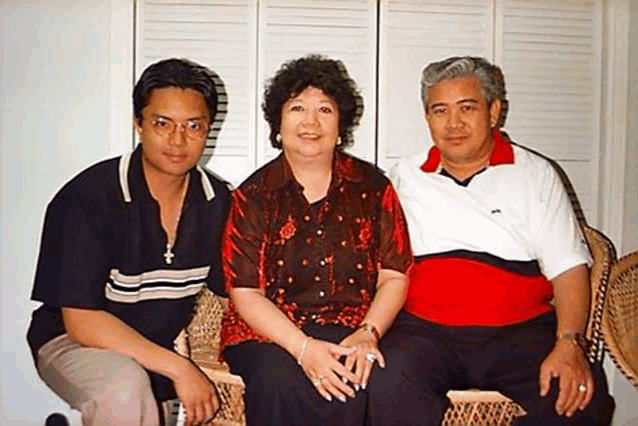 a man , a woman , and a man are posing for a picture while sitting in wicker chairs .