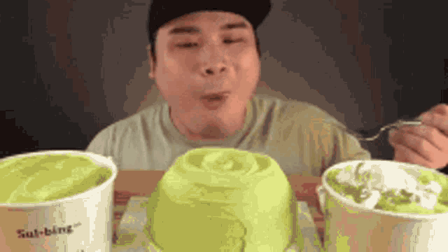 a man is sitting at a table eating ice cream from three different cups .