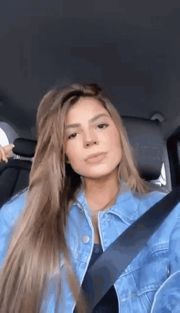 a woman in a denim jacket is sitting in a car with a seat belt .