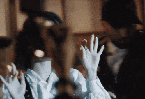 a woman wearing white gloves is waving her hands in front of a man