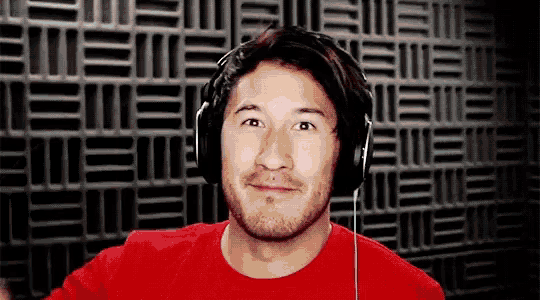 a man wearing headphones and a red shirt is smiling in front of a brick wall .
