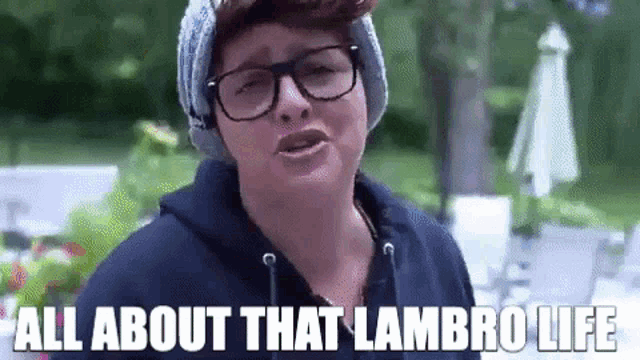 a man wearing glasses and a beanie is talking about all about that lambro life .