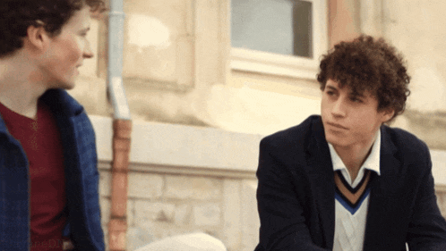 two young men are sitting next to each other talking