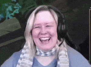 a woman wearing headphones and a scarf is smiling while sitting in front of a computer screen .