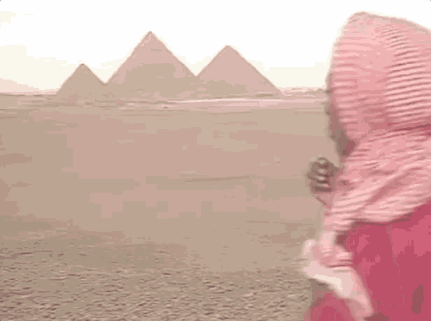 a man wearing a scarf and a red shirt is standing in front of the pyramids .